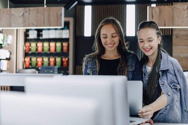 Chicas jóvenes atractivas en una tienda de electrónica utilizan una computadora portátil en una exposición