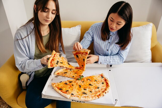 Chicas jóvenes comiendo pizza en casa