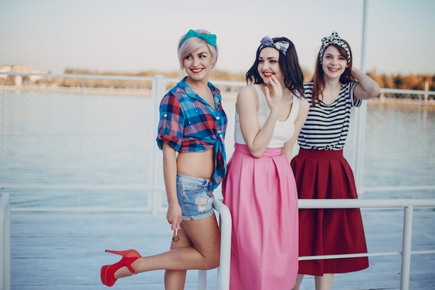 Chicas jóvenes posando en una barandilla de un puerto marítimo y una con una pierna levantada