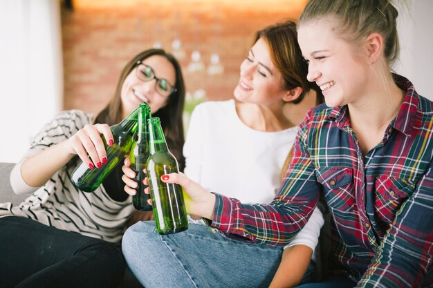 Chicas jóvenes tintinean con botellas de cerveza