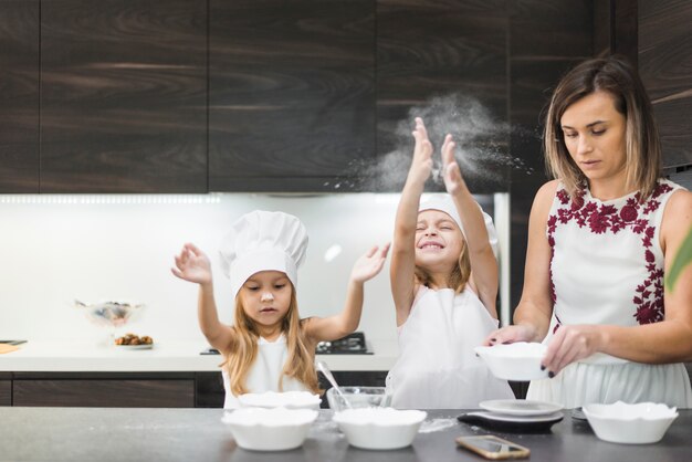 Chicas lindas disfrutando en la cocina mientras la madre prepara la comida.