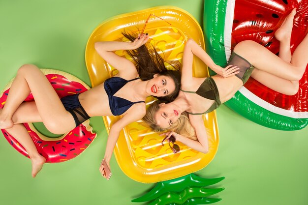 Chicas lindas en traje de baño posando en el estudio. Retrato de verano adolescentes caucásicos sobre un fondo verde.