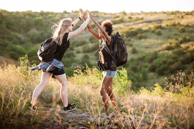 Chicas con mochilas sonriendo, dando cinco, viajando en el cañón