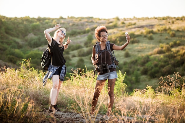 Chicas con mochilas sonriendo, haciendo selfie, viajando en el cañón