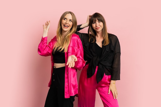 Chicas de moda sonrientes felices vistiendo elegante traje colorido, posando en la pared rosa