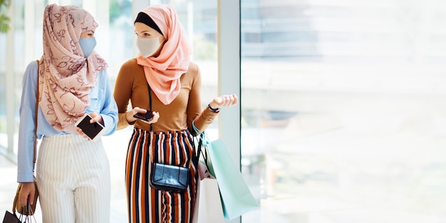 Chicas musulmanas en mascarilla de compras en el centro comercial en nueva normalidad