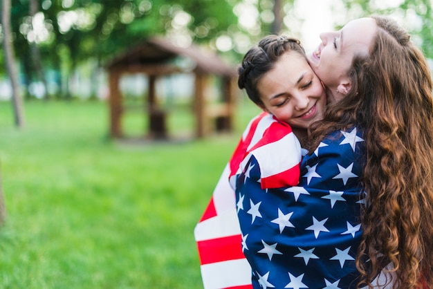 Chicas en la naturaleza abrazándose con bandera americana