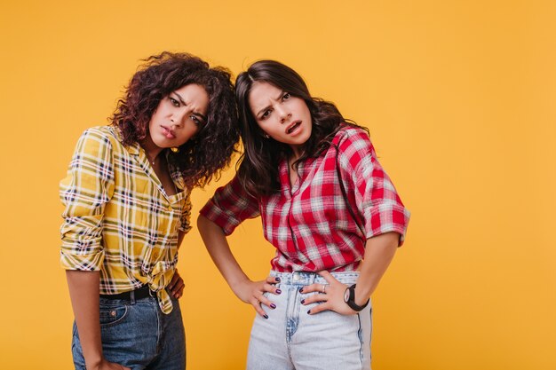 Las chicas de ojos marrones miran con indignación y condena. Instantánea de amigos descontentos con camisetas similares.