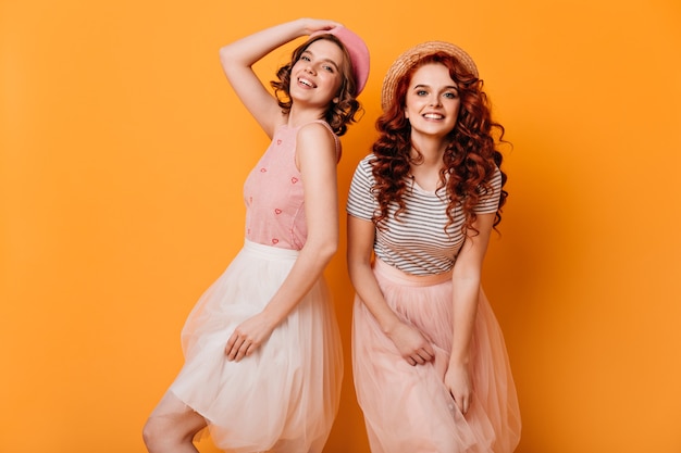 Chicas rizadas en faldas bailando sobre fondo amarillo. Foto de estudio de hermosas damas caucásicas expresando felicidad.