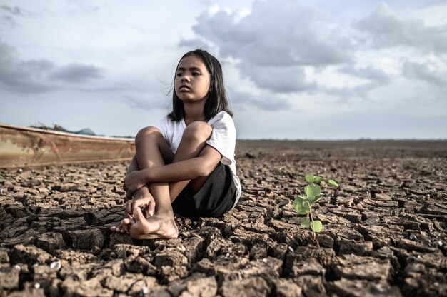 Chicas sentadas abrazando sus rodillas, mirando al cielo y teniendo árboles en tierra seca