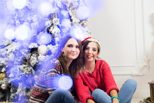 Chicas sentadas enfrente de árbol de navidad