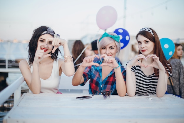 Chicas sentadas en una mesa sonriendo y haciendo corazones con las manos