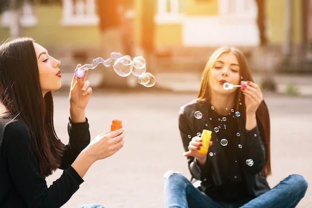 Chicas sentadas en el suelo soplando burbujas