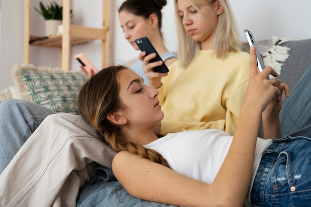 Chicas en el sofá con vista lateral de teléfonos inteligentes