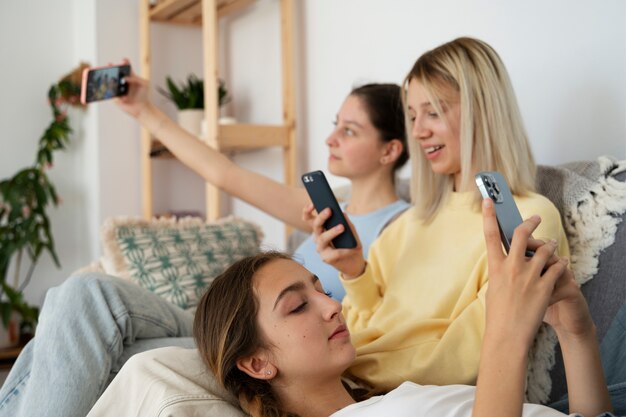 Chicas en el sofá con vista lateral de teléfonos inteligentes
