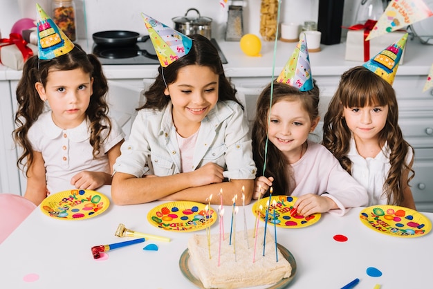 Foto gratuita chicas con sombreros de fiesta en la cabeza con platos de papel de cumpleaños en la mesa esperando el pastel de cumpleaños