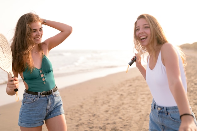 Chicas sonrientes sosteniendo la raqueta de tenis disfrutando en la playa