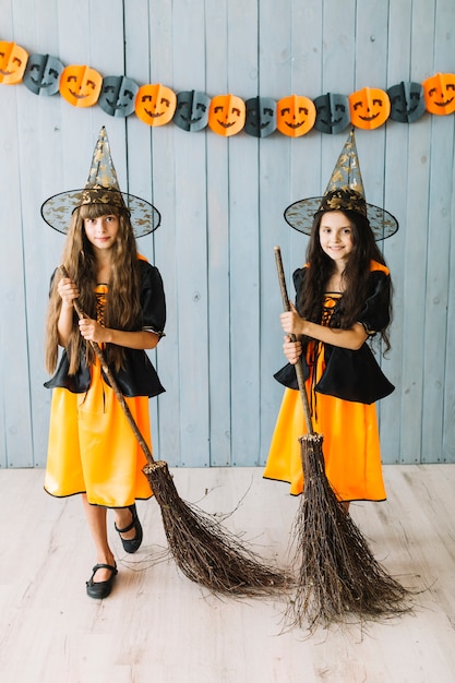 Chicas sonrientes en trajes de bruja posando con palos de escoba