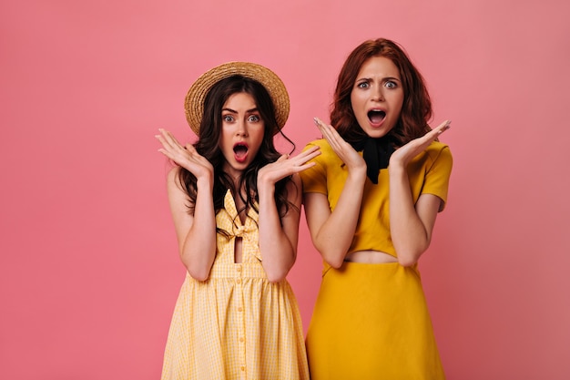 Chicas sorprendidas en trajes amarillos posando en la pared rosa