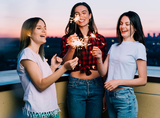 Foto gratuita chicas sosteniendo fuegos artificiales en la azotea al amanecer