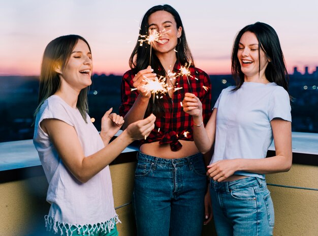 Chicas sosteniendo fuegos artificiales en la azotea al amanecer