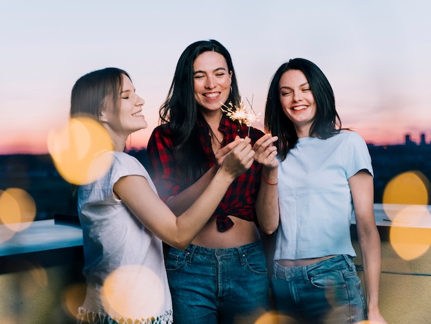 Foto gratuita chicas sosteniendo fuegos artificiales en la azotea al amanecer