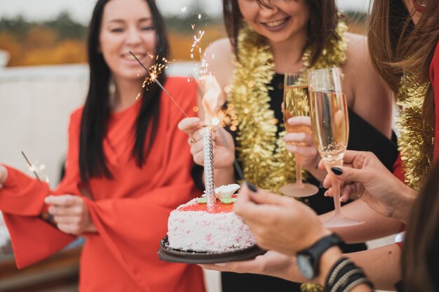 Chicas sosteniendo el pastel de cumpleaños y bengalas en una fiesta