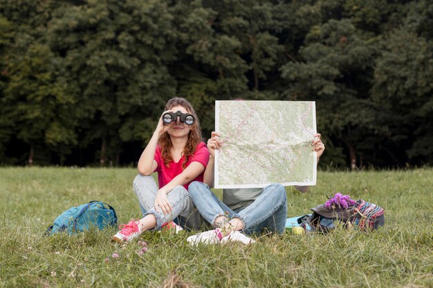 Chicas de tiro completo con binoculares y mapa.