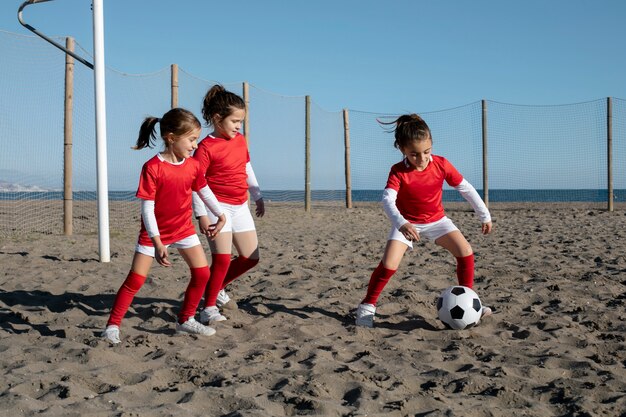 Chicas de tiro completo jugando al fútbol en la playa