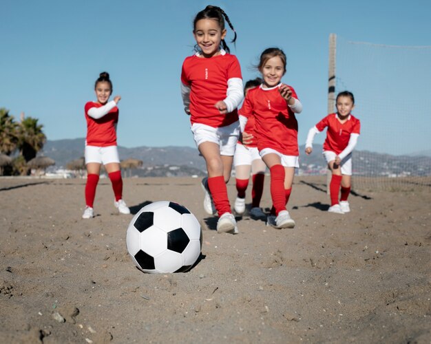 Chicas de tiro completo jugando al fútbol en la playa