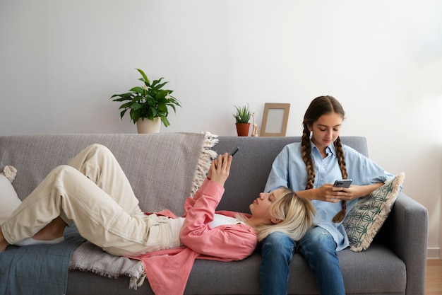 Foto gratuita chicas de tiro completo en el sofá con teléfonos inteligentes