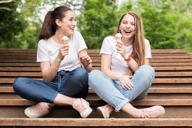 Chicas de tiro largo que tienen un helado en las escaleras