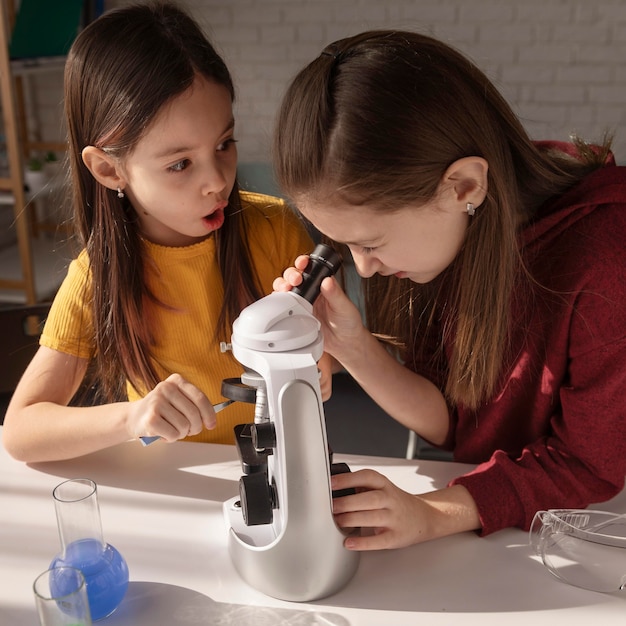 Chicas de tiro medio aprendiendo con microscopio.