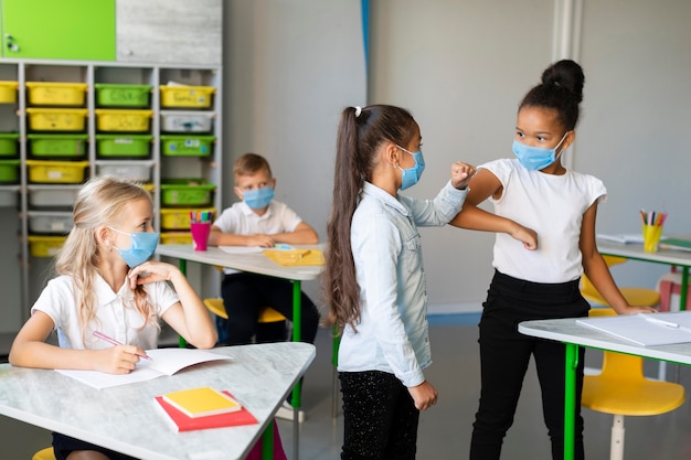 Chicas de tiro medio golpeando el codo en clase