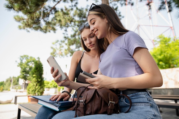 Chicas de tiro medio con libros y teléfonos inteligentes.