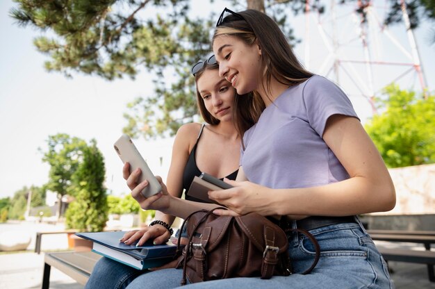 Chicas de tiro medio con libros y teléfonos inteligentes.