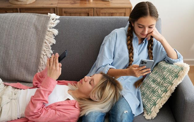 Chicas de tiro medio en el sofá con teléfonos inteligentes