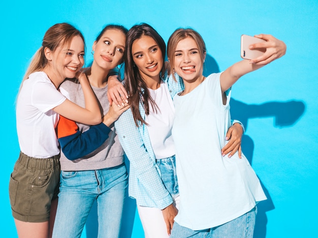 Chicas tomando fotos de autorretrato autofoto en smartphone.Modelos posando cerca de la pared azul en el estudio, hembra mostrando emociones positivas