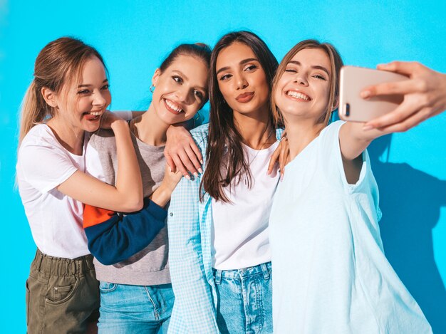 Chicas tomando fotos de autorretrato autofoto en smartphone.Modelos posando cerca de la pared azul en el estudio, hembra mostrando emociones positivas