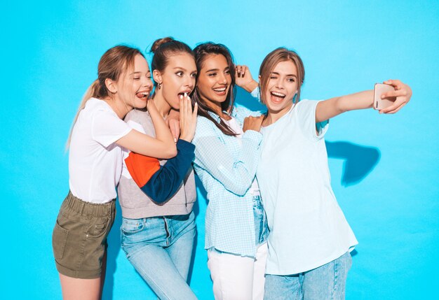 Chicas tomando fotos de autorretrato autofoto en smartphone.Modelos posando cerca de la pared azul en el estudio, hembra mostrando emociones positivas