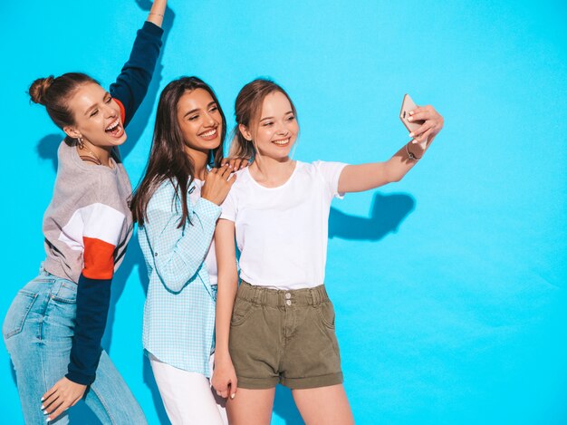 Chicas tomando fotos de autorretrato selfie en smartphone.Modelos posando junto a la pared azul en el estudio.