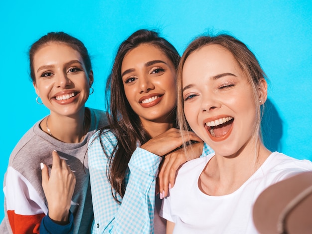 Chicas tomando fotos de autorretrato selfie en smartphone.Modelos posando junto a la pared azul en el estudio.