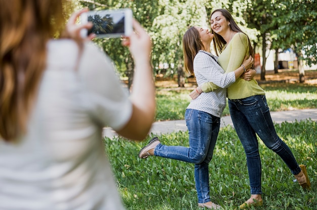 Chicas tomando fotos mientras se besan en la mejilla