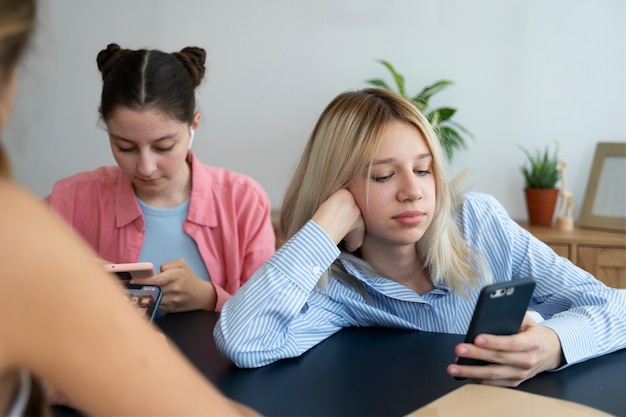 Chicas de vista frontal sentadas con teléfonos inteligentes