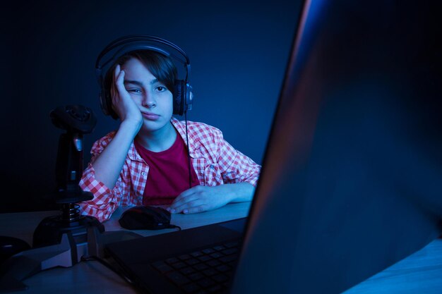 chico aburrido No quiere dormir después de jugar videojuegos toda la noche. En la luz azul de la pantalla, los niños emocionales juegan juegos de computadora en línea.