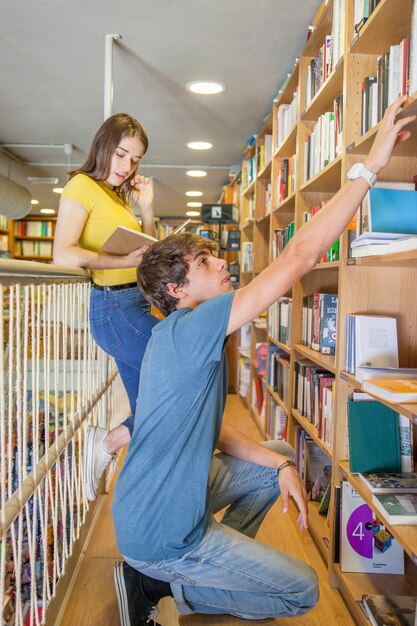 Chico adolescente alcanzando estante mientras busca libro cerca de novia