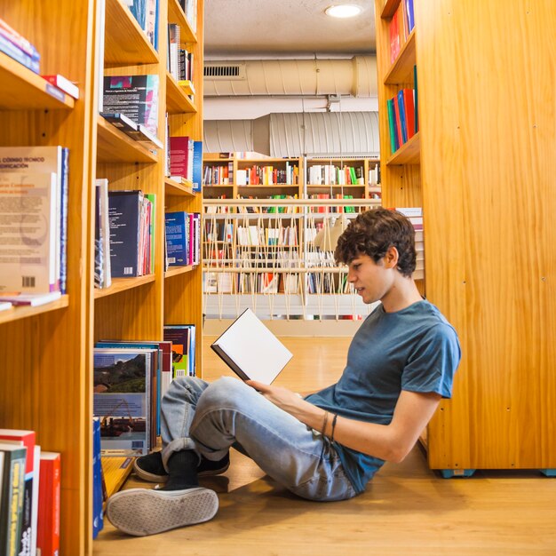 Chico adolescente apoyado en librería y leyendo