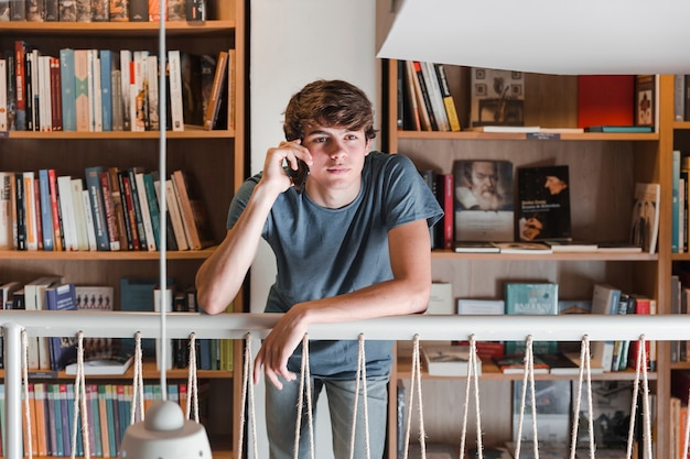 Chico adolescente hablando en teléfono inteligente en la biblioteca