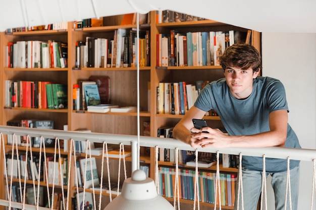 Chico adolescente con teléfono inteligente en la biblioteca