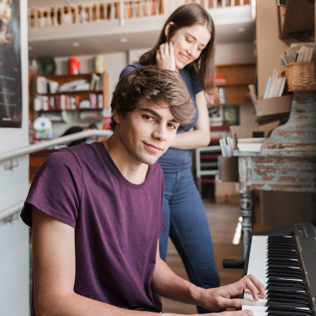 Chico adolescente tocando el piano para novia en la habitación acogedora